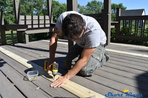 Kneeling on an existing deck to fasten a new board with a drill