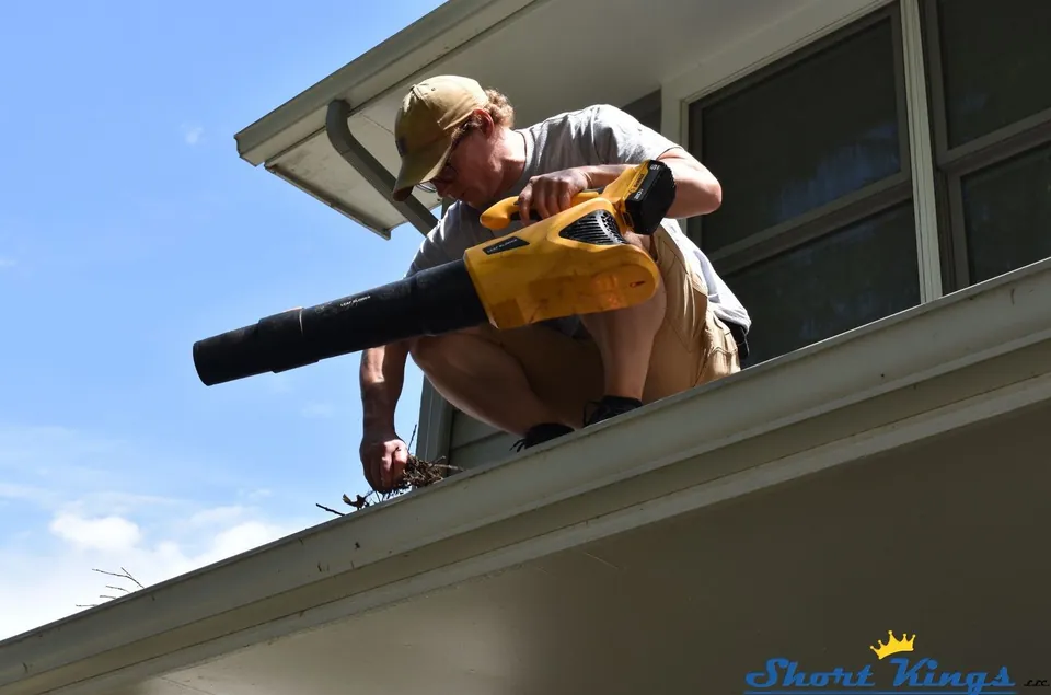 Cleaning a gutter with a yellow blower at the roof edge