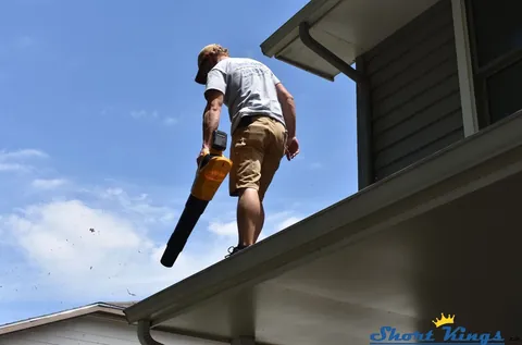 Using a yellow blower to clear a gutter from the roof edge